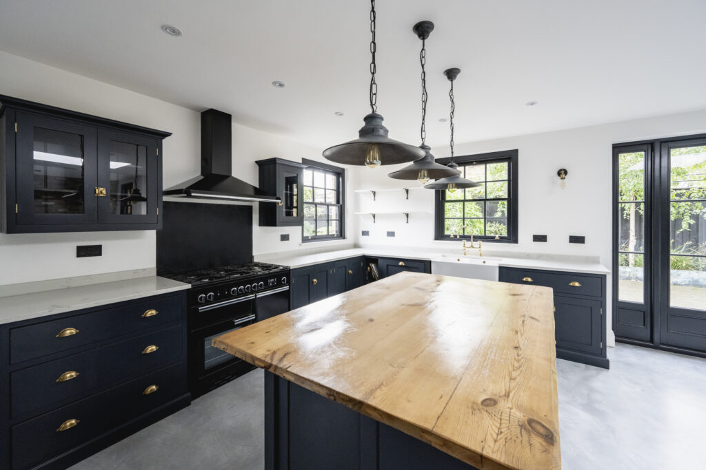 5 Key Remodeling Trends in Northern VA (2025) Black cabinets, reclaimed wood countertop, pendant lights, black accented cabinets and appliances, and access to outdoor patio.